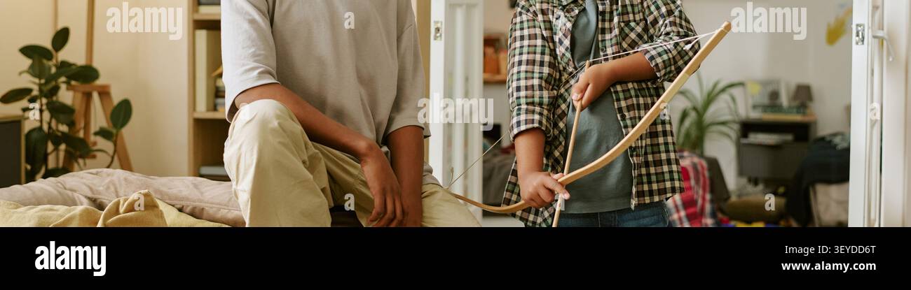 Intestazione di teenager e bambino che giocano con Bow and Arrow a casa Foto Stock