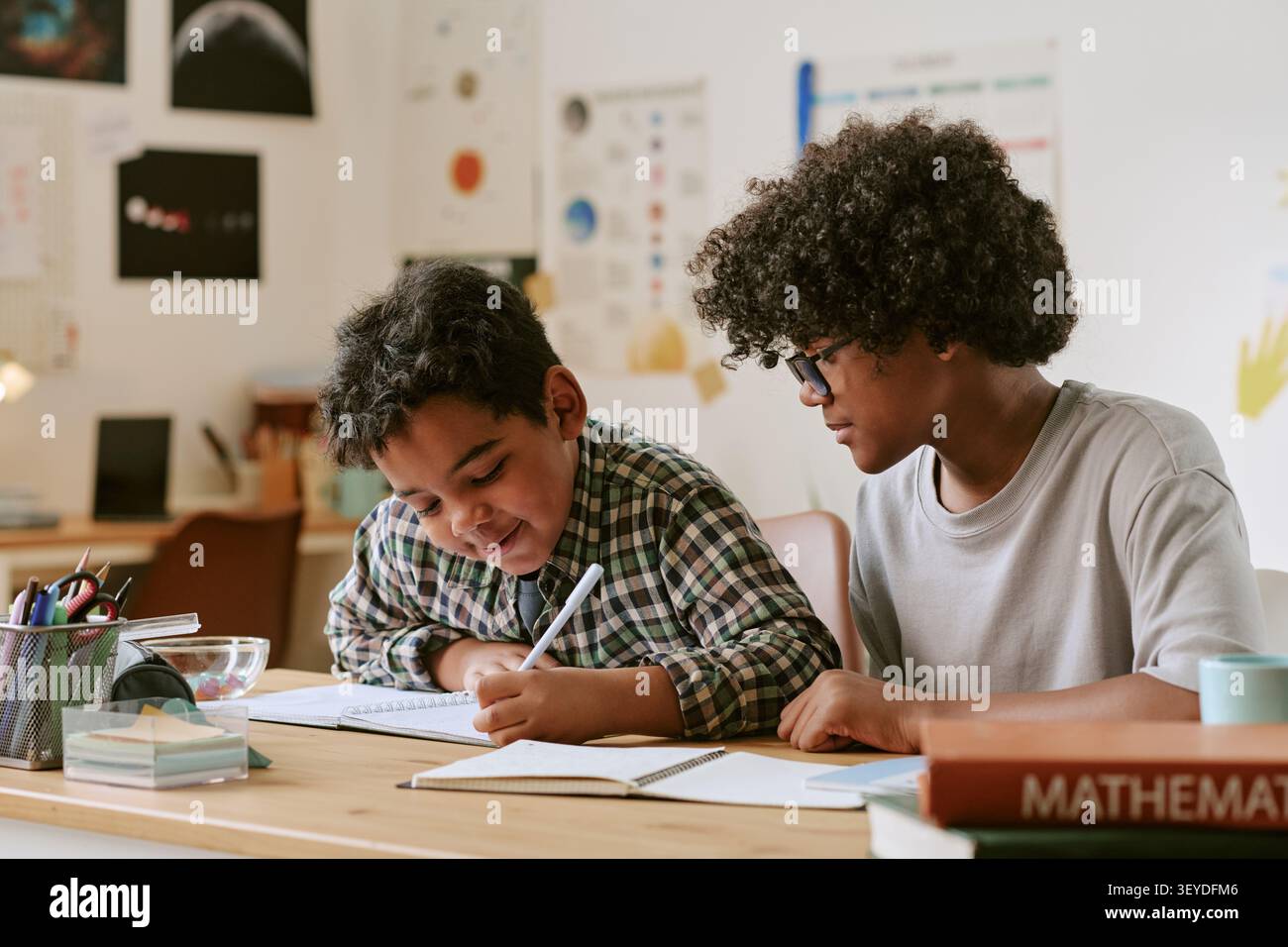Black Teenager Tutoring Child che scrive in una sessione di studio a casa Foto Stock
