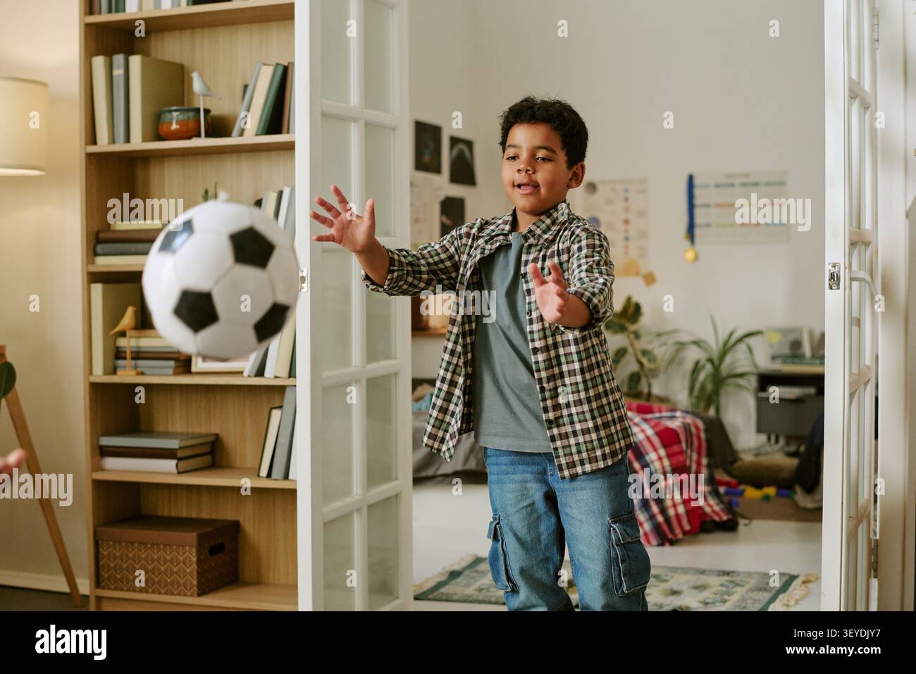 Black Boy che cattura il pallone da calcio durante il gioco in famiglia al coperto Foto Stock