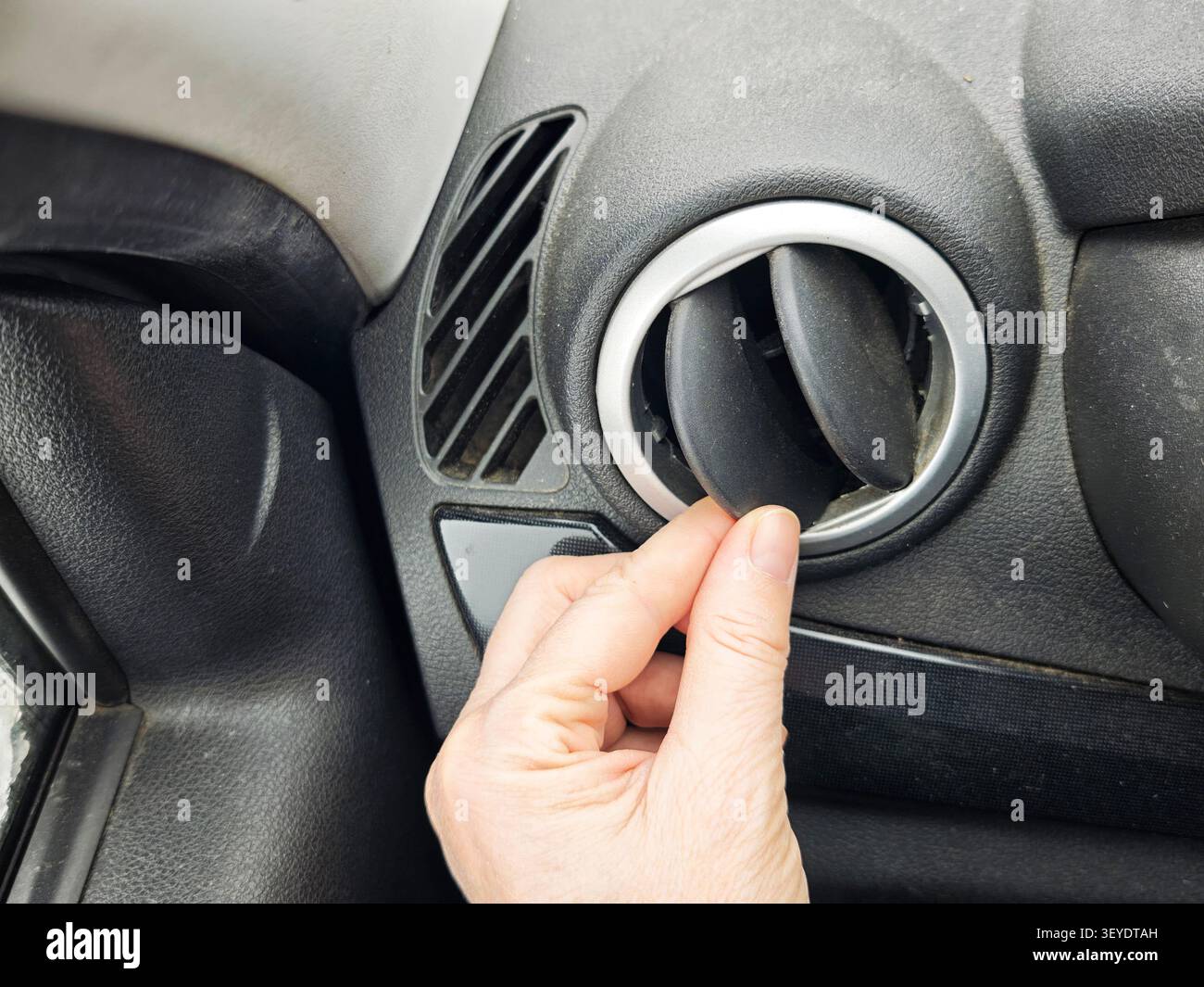 Una mano si avvicina per regolare la presa d'aria in un'auto come preparazione per un viaggio. Gli interni dell'auto mostrano segni di preparazione al viaggio. Foto Stock
