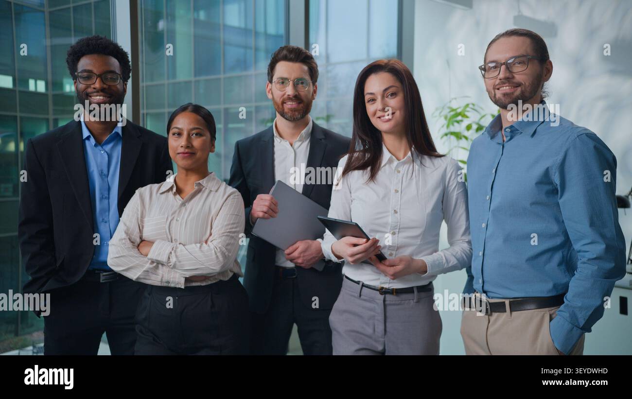 Team aziendale multietnico felice che si posa in ufficio insieme. Cinque colleghi d'affari multirazziali che sorridono guardando la telecamera dell'azienda. Allegro Foto Stock