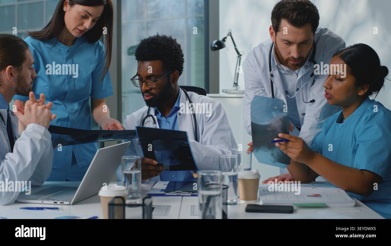 Team di medicina internazionale che analizza il cancro ai raggi X polmoni diagnosi di pandemia covid collaborazione parlante in clinica moderna. Cinque medici multirazziali parlano Foto Stock