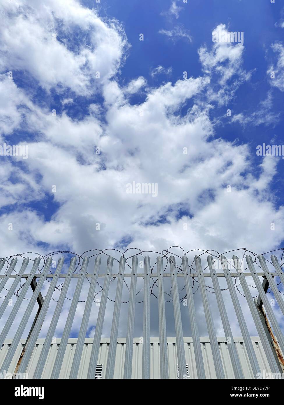 Barriera e filo spinato contro un cielo blu nuvoloso, Wigan - Immagine stock catturata con smartphone