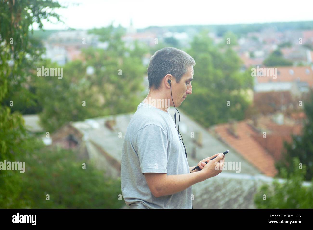 Uomo che ascolta attraverso gli auricolari mentre controlla lo smartphone all'aperto. Apprendimento audio mobile, educazione autodirezionale e produttività digitale focalizzata. Foto Stock