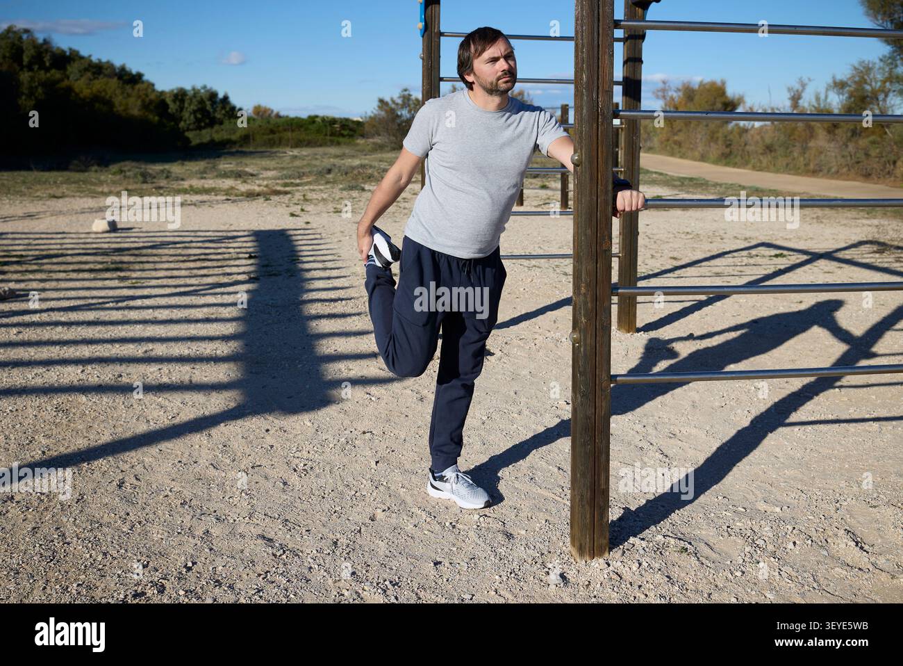 Uomo che si allunga sulle barre di allenamento all'aperto durante una sessione di allenamento al sole. Foto Stock