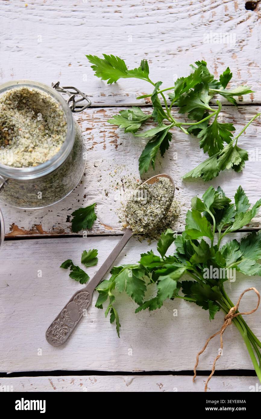 Ciuffi di prezzemolo freschi con sale stagionato in cucchiaio su fondo rustico in legno bianco Foto Stock