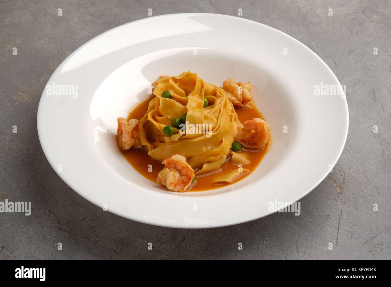 Elegante nido di gamberi con piselli e ricca salsa d'arancia su piatto bianco Foto Stock