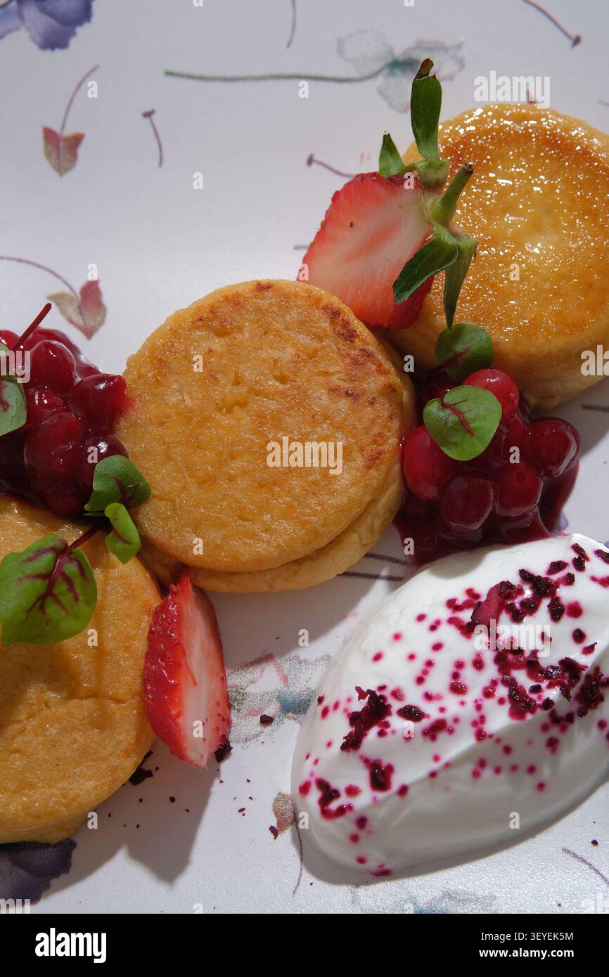 Frittelle dorate con panna montata, fragole, salsa di bacche e menta su un piatto a motivi geometrici Foto Stock