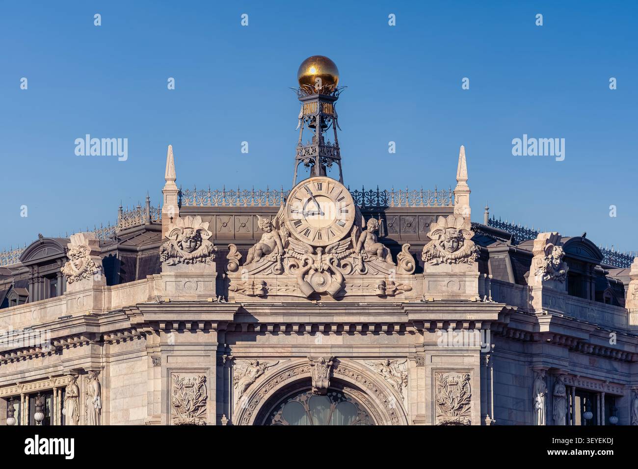 Facciata superiore della Banco de Espana che mette in evidenza l'orologio monumentale e i dettagli architettonici del tetto a Madrid Foto Stock