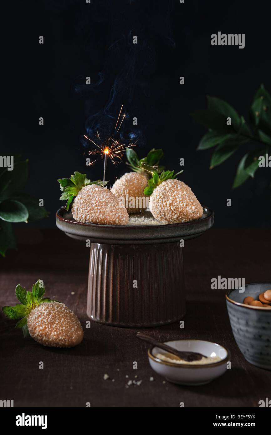 Espositore per dessert con dolci ricoperti di sesamo su piedistallo, scintillante, sfondo scuro Foto Stock