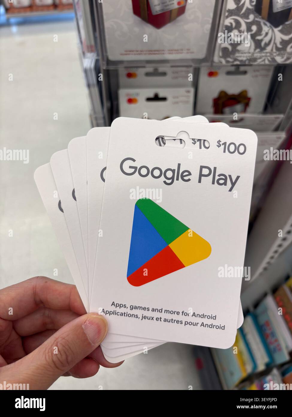 Primo piano di una persona che detiene più buoni regalo del negozio Google Play in un ambiente di vendita al dettaglio con prodotti sfocati sullo sfondo. Foto Stock