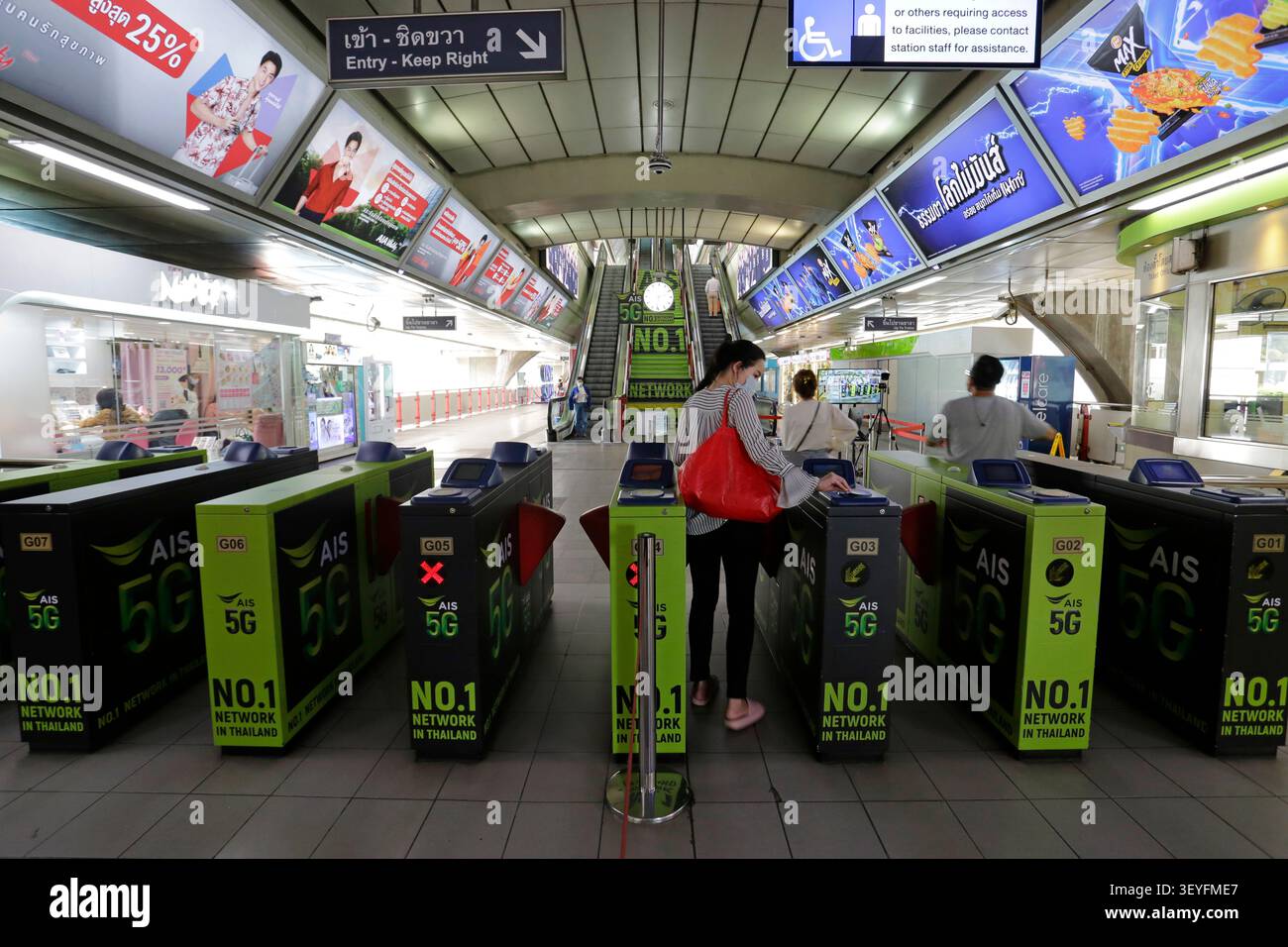 Bangkok, Tailandia - 4 luglio 2022: Le persone passano accanto agli annunci di AIS, Advanced Info Service PLC, compagnia di telefonia mobile, nella stazione ferroviaria Siam BTS. Foto Stock