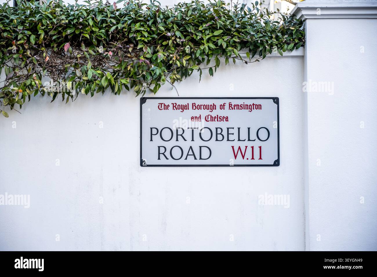 Un chiaro cartello stradale per "PORTOBELLO ROAD W.11", montato su una parete bianca sotto il verde del fogliame nel Royal Borough di Kensington e Chelsea, London, U Foto Stock