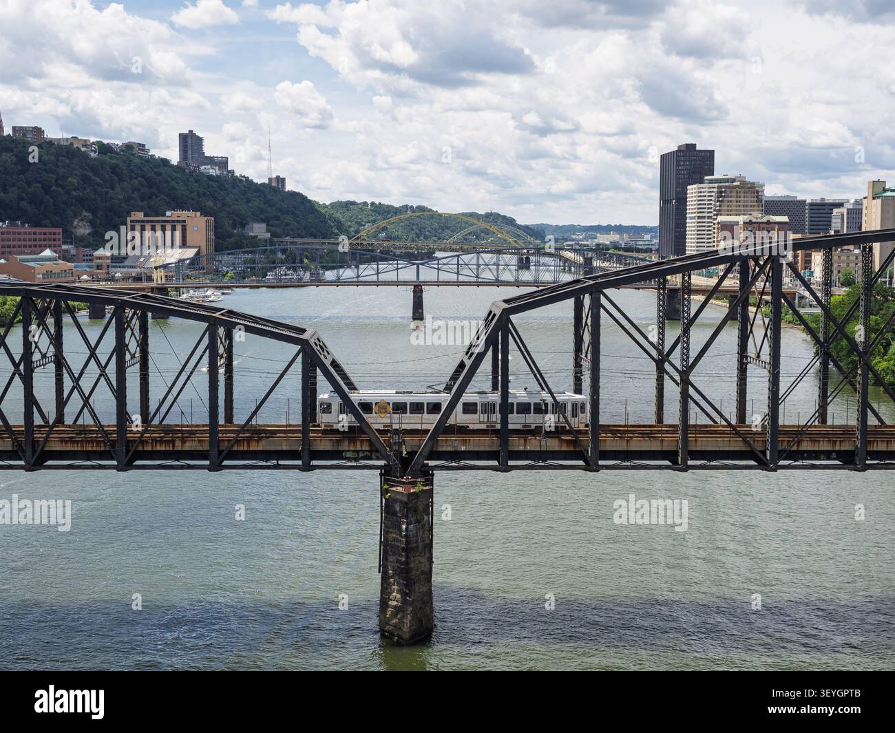 Pittsburgh Pennsylvania-06 21 2026: Veduta profilo di un'auto pendolare di transito della ferrovia leggera che attraversa uno storico ponte di ferro su un fiume. Foto Stock