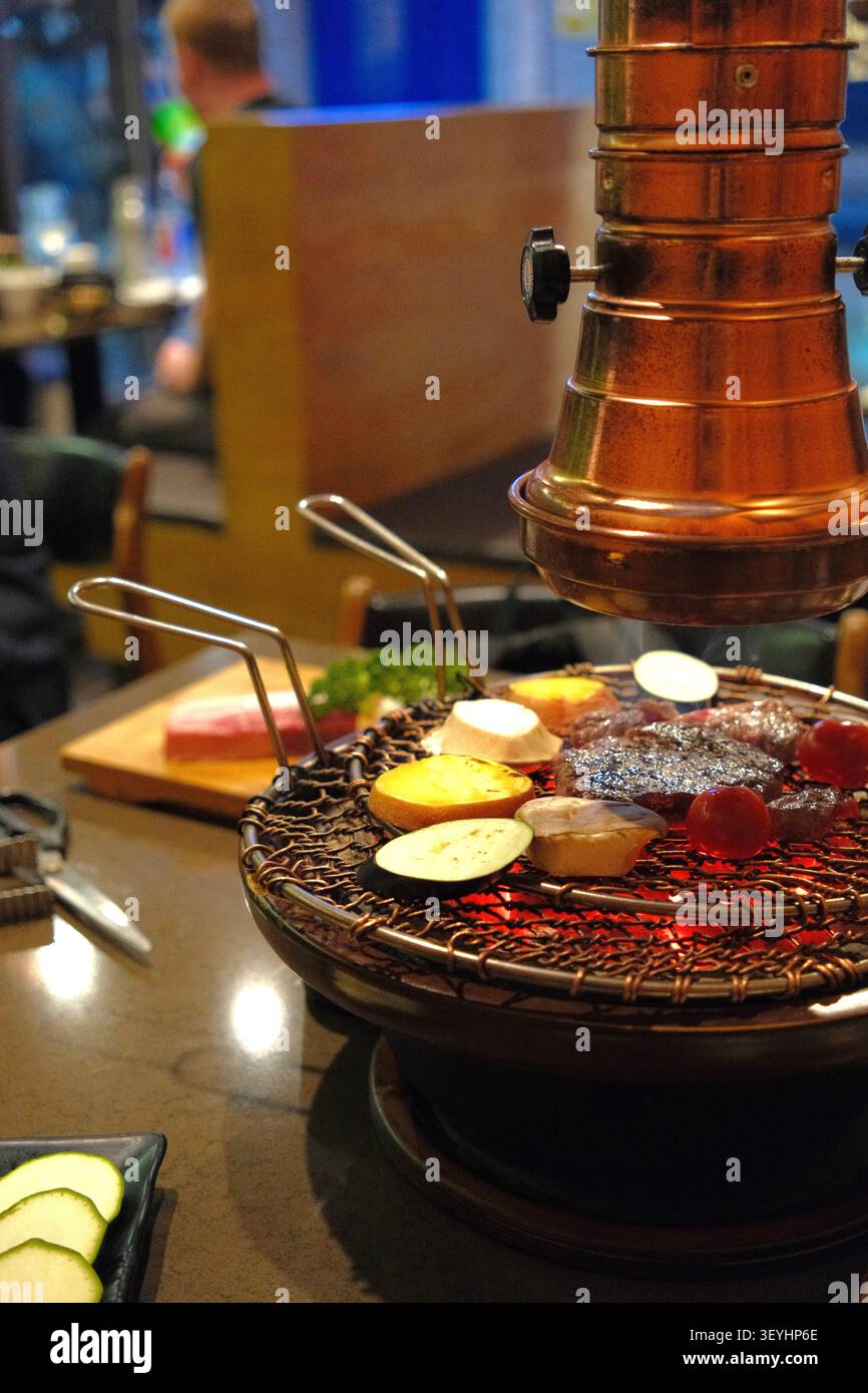 BBQ coreano: carne e verdure grigliate sul carbone su un grill da tavolo con cappa di scarico in rame in un ristorante a Seoul, Corea del Sud Foto Stock