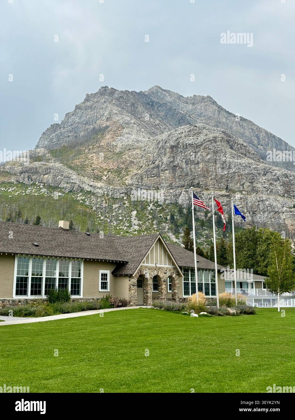 Edificio con bandiere che volano nel sito della città di Waterton, sullo sfondo di una montagna, il Waterton Lakes National Park, Alberta, Canada. - Immagine stock catturata con smartphone