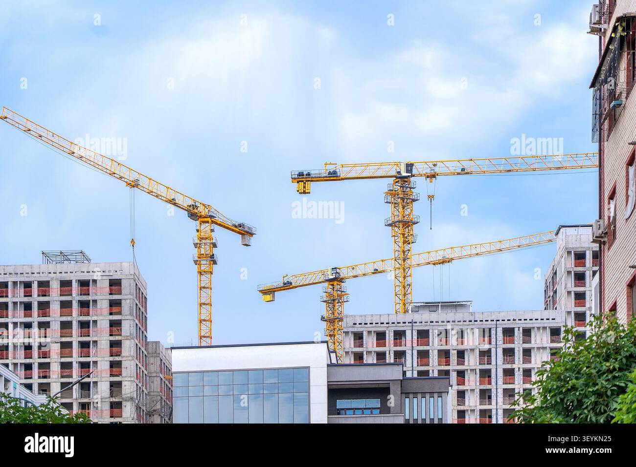 Macchinari per l'edilizia pesante e gru a torre che lavorano nelle immediate vicinanze di un edificio residenziale. Concetto: Disagio urbano e inquinamento atmosferico Foto Stock