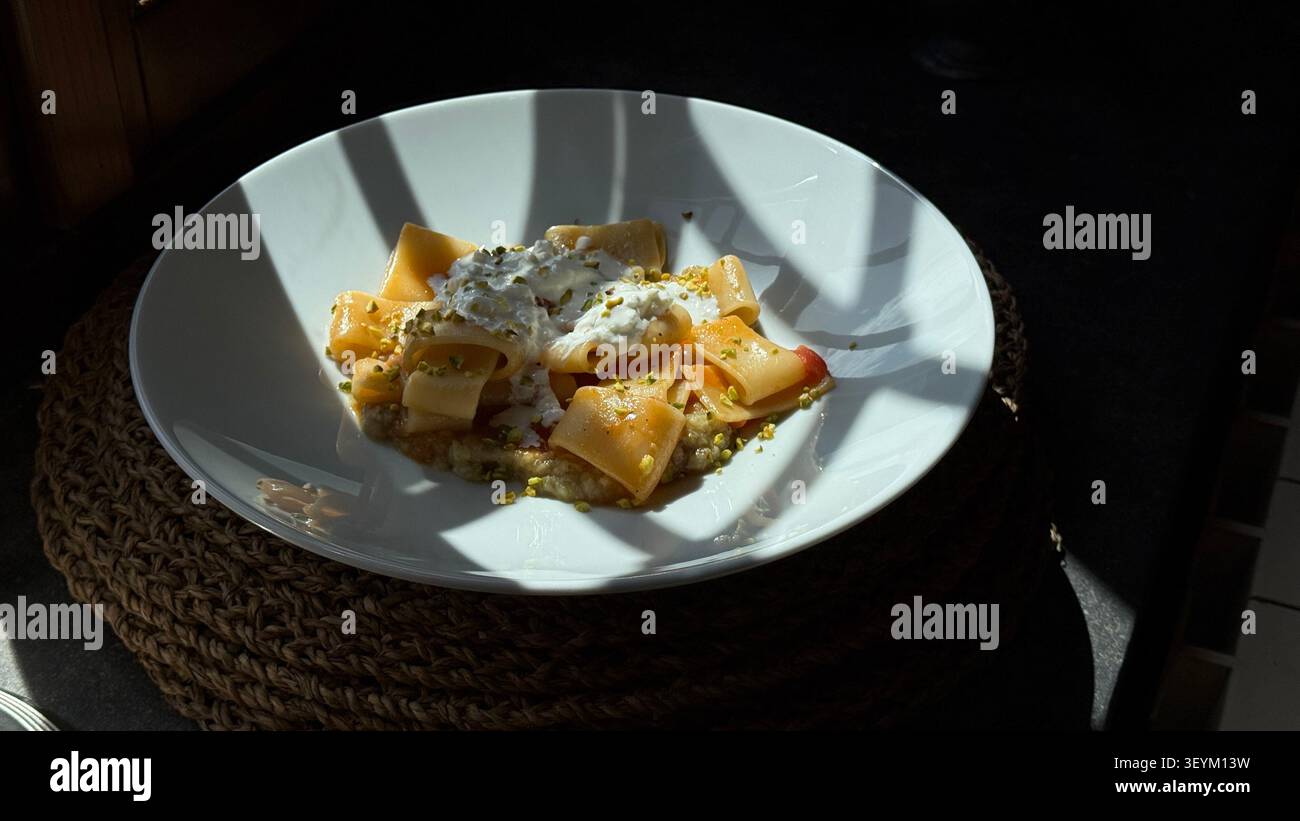 Deliziosa pasta gourmet condita con salsa cremosa e pistacchi, servita in un'elegante ciotola bianca. Il piatto è esposto artisticamente alla luce solare Foto Stock