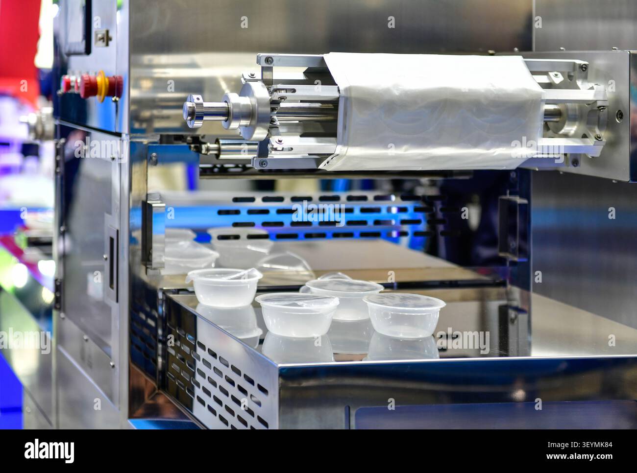 Macchina automatica per la sigillatura e l'imballaggio di vassoi di plastica in funzione in una fabbrica alimentare industriale Foto Stock