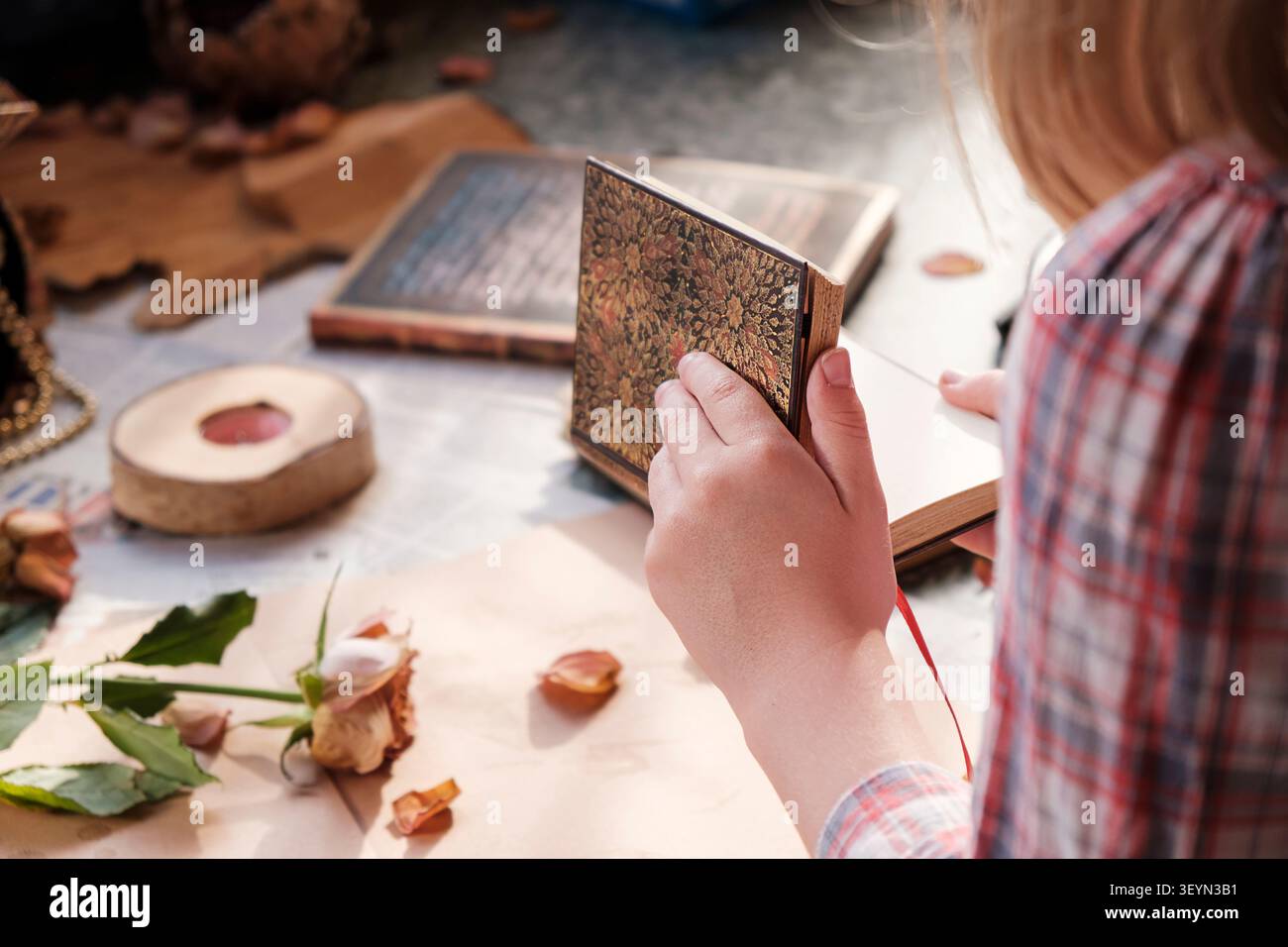 Bambino che apre un quaderno bianco d'epoca circondato da rose essiccate e una chiave antica. Un concetto di narrazione accogliente, creatività e immaginazione. Foto Stock