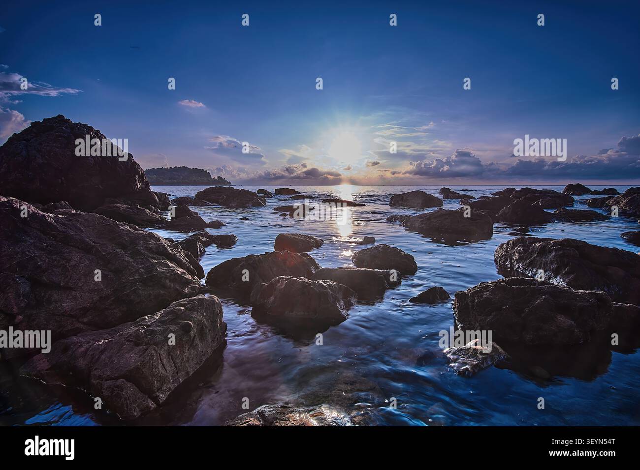 Il sole sorge sull'orizzonte al mare, su una spiaggia rocciosa. Le onde si infrangono sulle rocce, creando uno spettacolo bellissimo Foto Stock