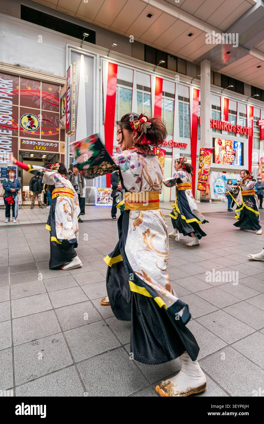Due file di giovani ballerine giapponesi sorridenti con maniche lunghe vorticose durante un evento di danza Yosakoi in scena in una galleria di negozi a Kumamoto. Foto Stock