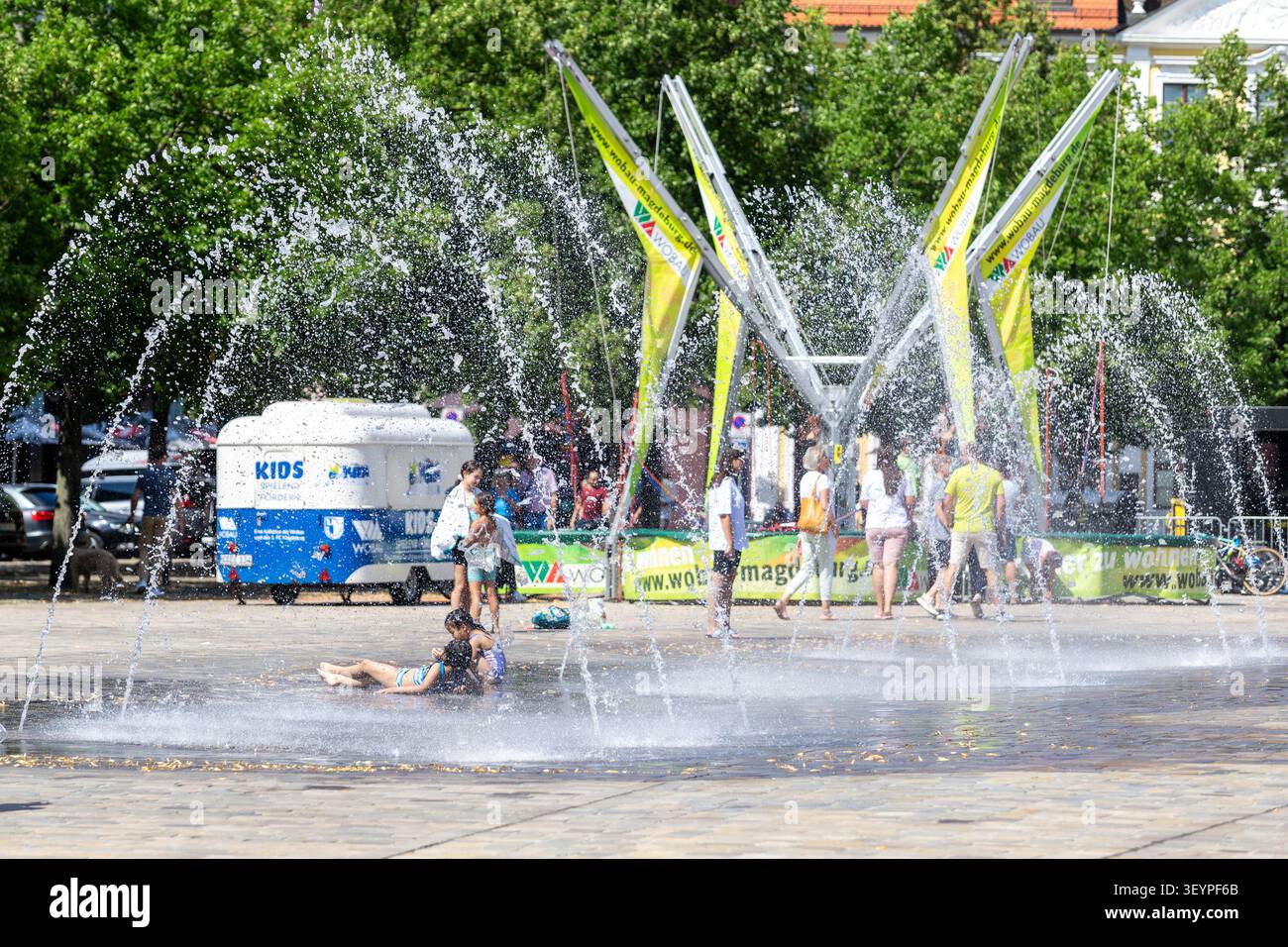 Magdeburgo, Germania - 23 luglio 2022. Domplatz People rinfrescante fontana spruzza caldi pedoni della giornata estiva striscioni WOBAU nelle vicinanze. Vista sulla città editoriale Foto Stock