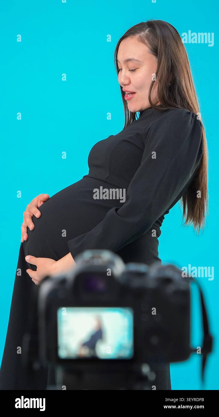 Donna incinta che filma video per blog su sfondo blu Foto Stock