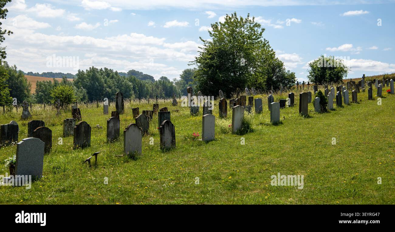 Un cimitero rurale tranquillo con file di antiche lapidi consumate su una collina erbosa sotto un cielo blu brillante con nuvole sparse Foto Stock
