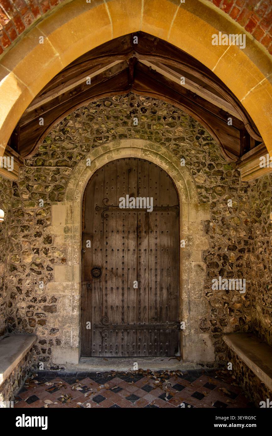 Una porta ad arco in legno antica inserita in un portico storico in pietra con pareti in selce e un arco decorativo in pietra Chiesa di San Pietro Over Wallop Foto Stock