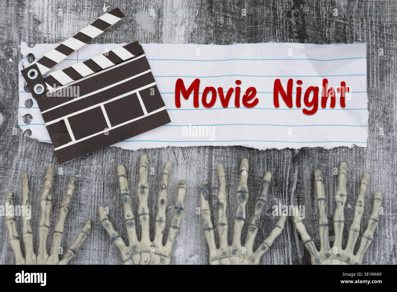 Movie Night text con due paia di scheletro mani su carta strappata e clapper cinematografico su legno intempestivo per una maratona di film horror Foto Stock