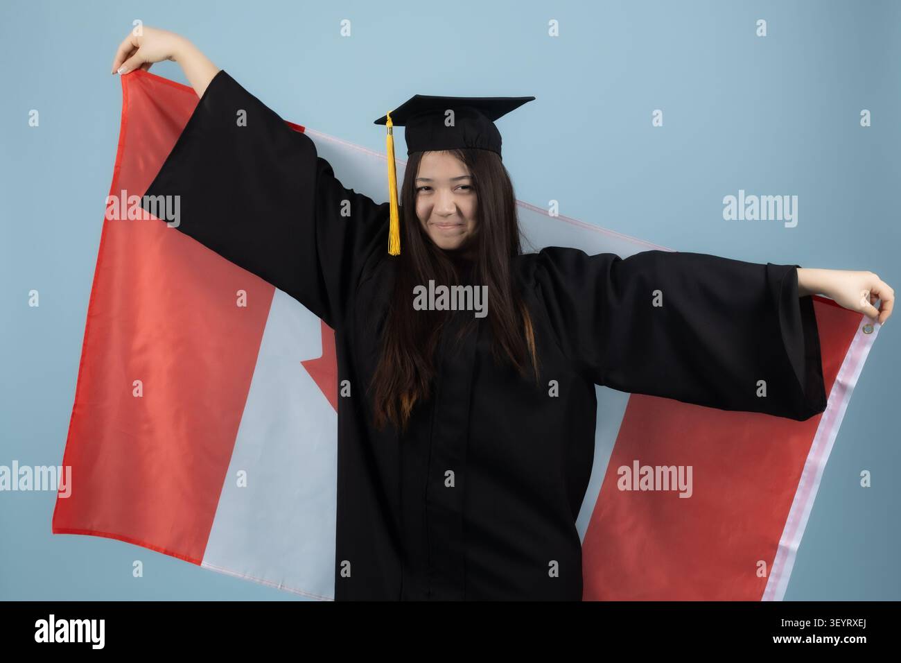 Giovane donna in abito da laurea a braccia aperte che celebra il successo Foto Stock