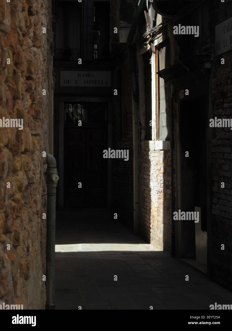 Vicolo stretto e scuro a Venezia, Italia, con un raggio di luce solare che illumina le pareti in mattoni Foto Stock