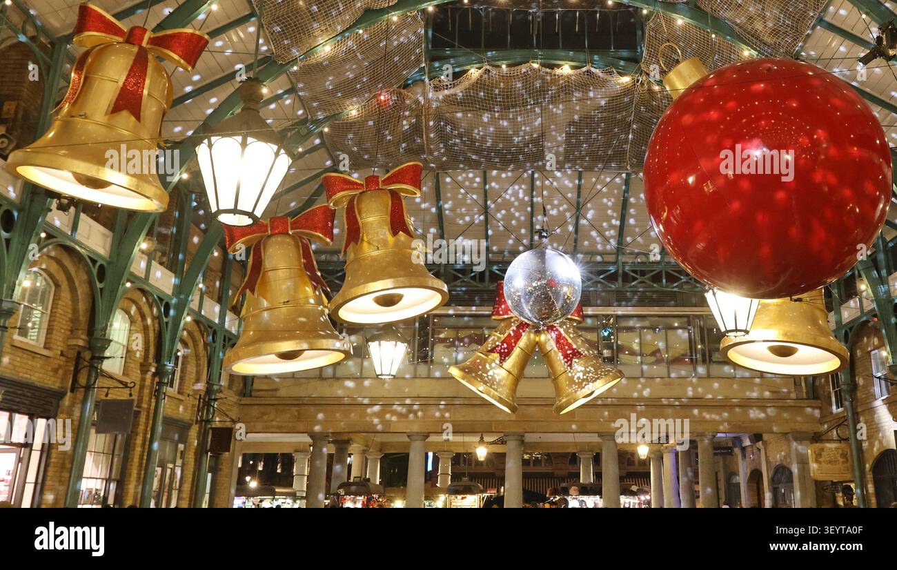 Una sala giochi interna decorata a festa o un mercato coperto pieno di decorazioni natalizie. Grandi campane dorate con archi rossi pendono dal metallo arcuato c Foto Stock