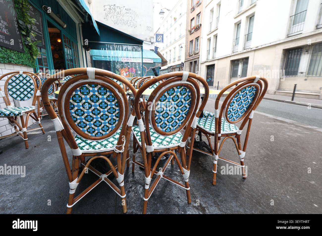 Les chaises en rotin sont mises autour d'une table dans un ristorante. La rue est calme et les bâtiments sont typiques de Paris. conv. Est. L'atmosphère Foto Stock