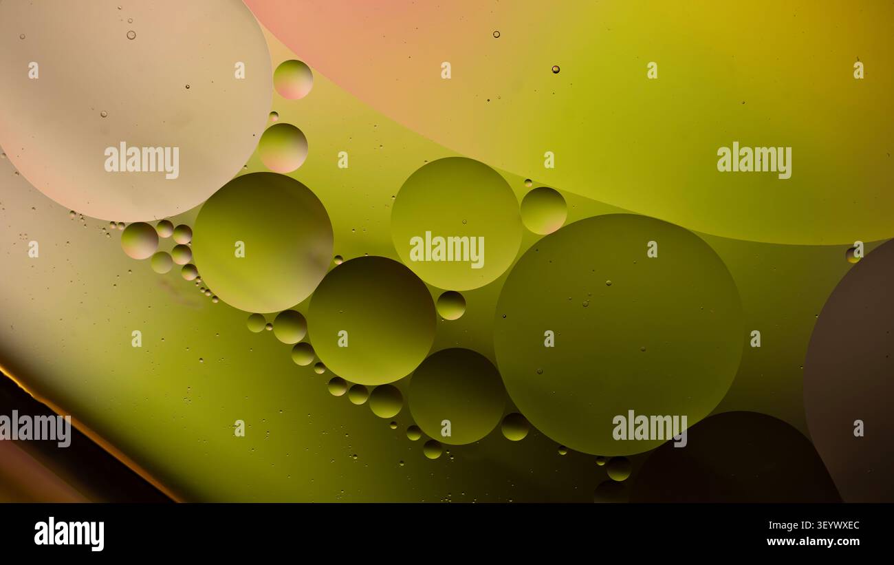 Vista ravvicinata delle goccioline d'olio sospese in un liquido colorato con sfumature verdi e gialle, creando una scena astratta adatta all'arte e al design Foto Stock