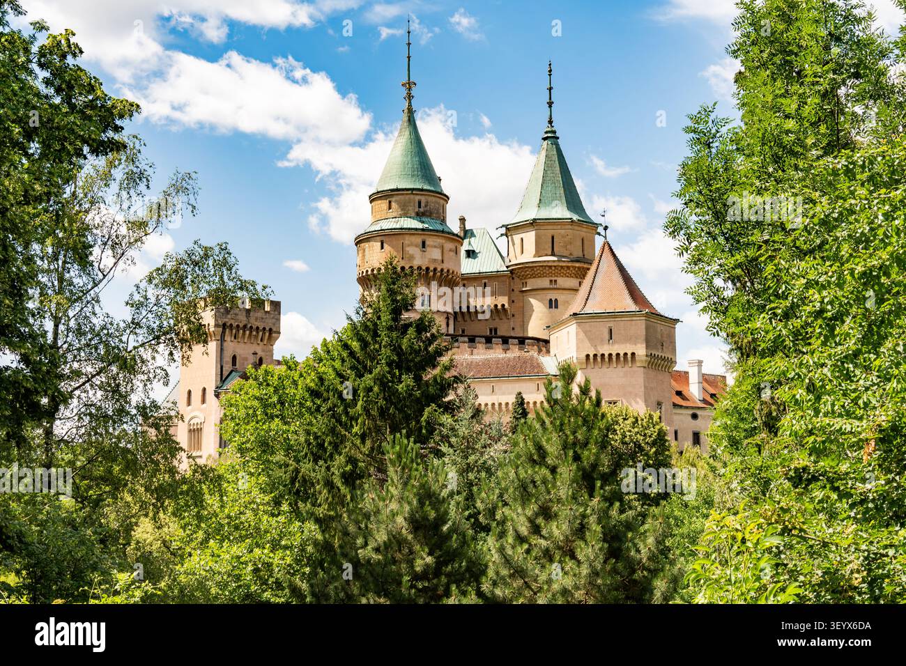 Le torri del castello di Bojnice si innalzano sopra le verdi cime degli alberi estive sotto un cielo blu, in Slovacchia Foto Stock