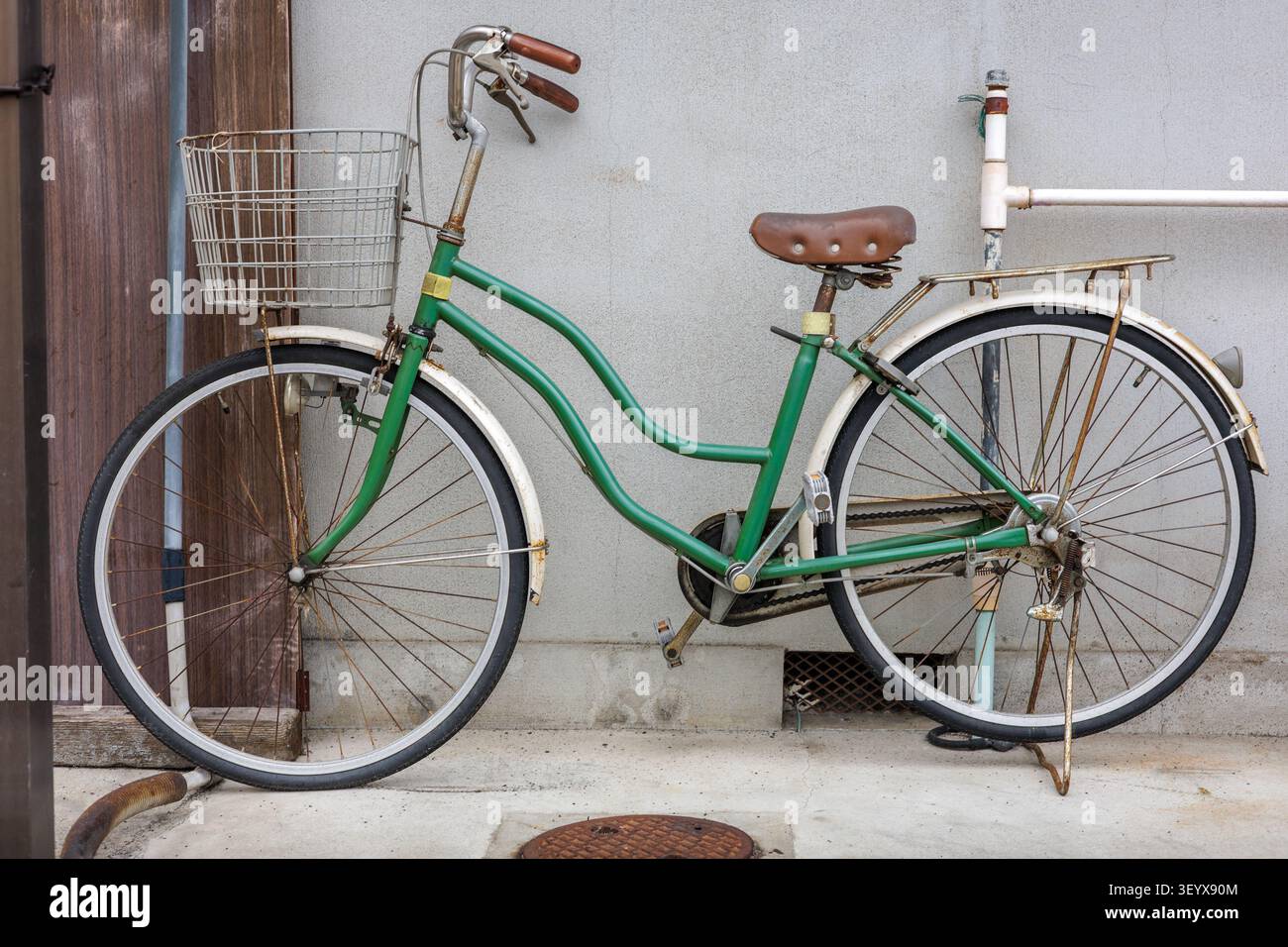 Bicicletta utilitaria giapponese mamachari verde vintage con telaio a passo, parcheggiata su un cavalletto a doppio lato davanti a un muro di cemento. Foto Stock