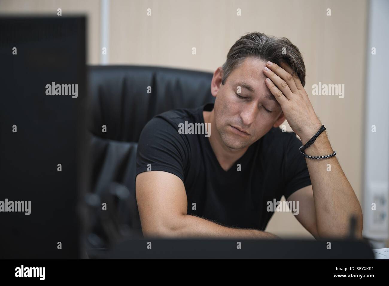 Fatica e burnout sul posto di lavoro. Uomo stanco e stressato alla scrivania che si tiene la testa. Foto Stock