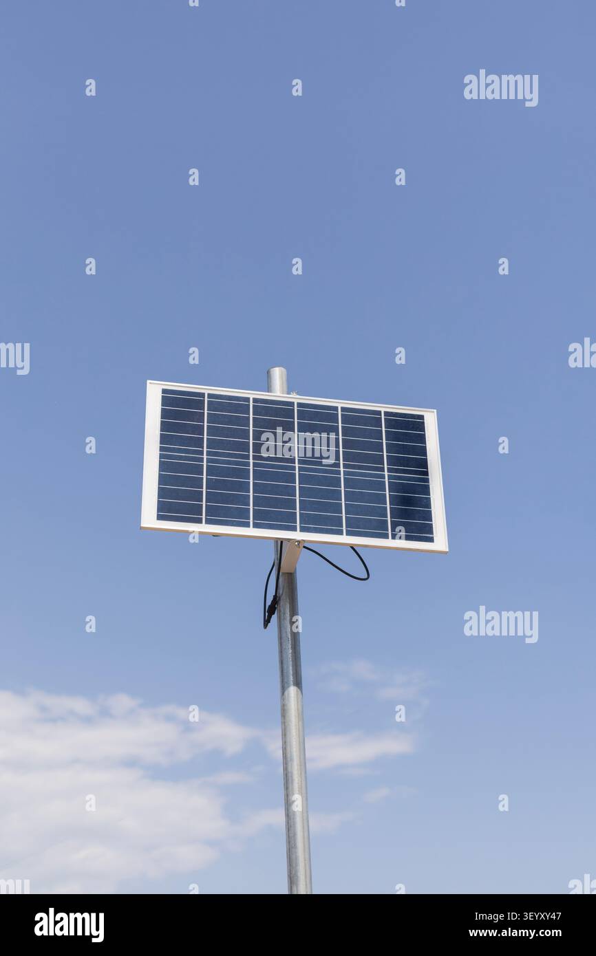 Un singolo pannello solare è montato su un palo metallico. Il pannello è rivolto verso il sole sotto un cielo blu chiaro con alcune nuvole di luce nella parte inferiore. Foto Stock