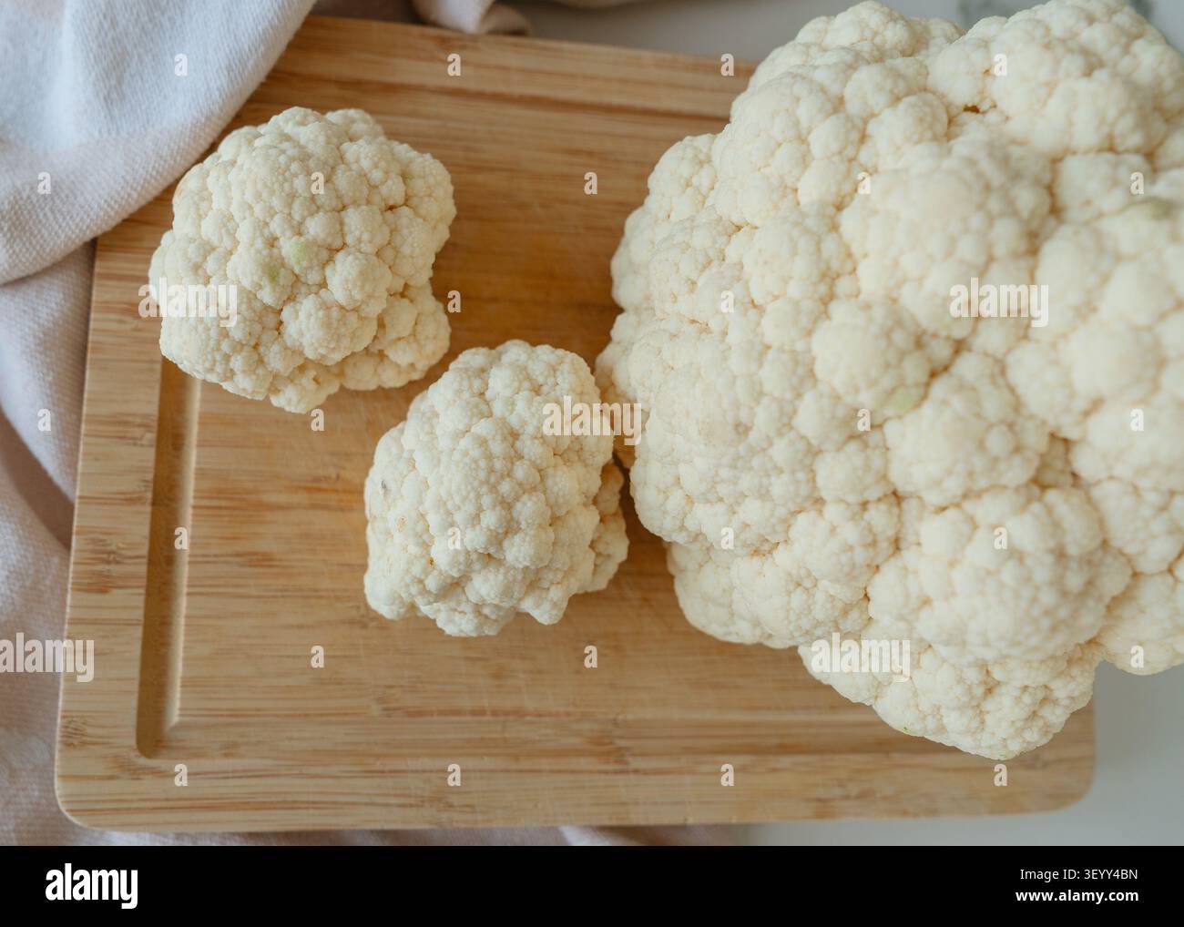 Un'esposizione statica di cavolfiore pulita su un tagliere in legno, completata da un asciugamano da cucina, catturato da una prospettiva dall'alto verso il basso. Questa immagine lo è Foto Stock