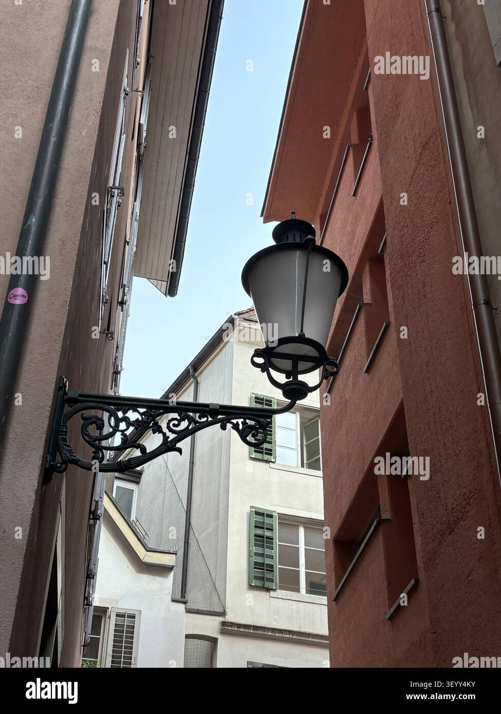 Un classico lampione in ferro battuto fissato a un vecchio muro di un edificio cittadino in un vicolo stretto, Zurigo - Immagine stock catturata con smartphone