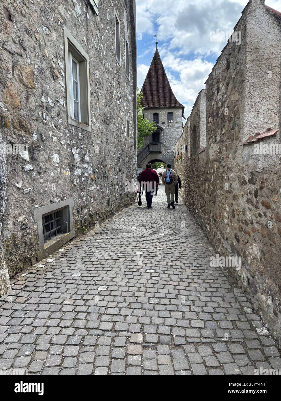 Turisti che camminano lungo una stretta via storica lastricata di ciottoli verso un'antica porta torre in pietra in Svizzera - Immagine stock catturata con smartphone