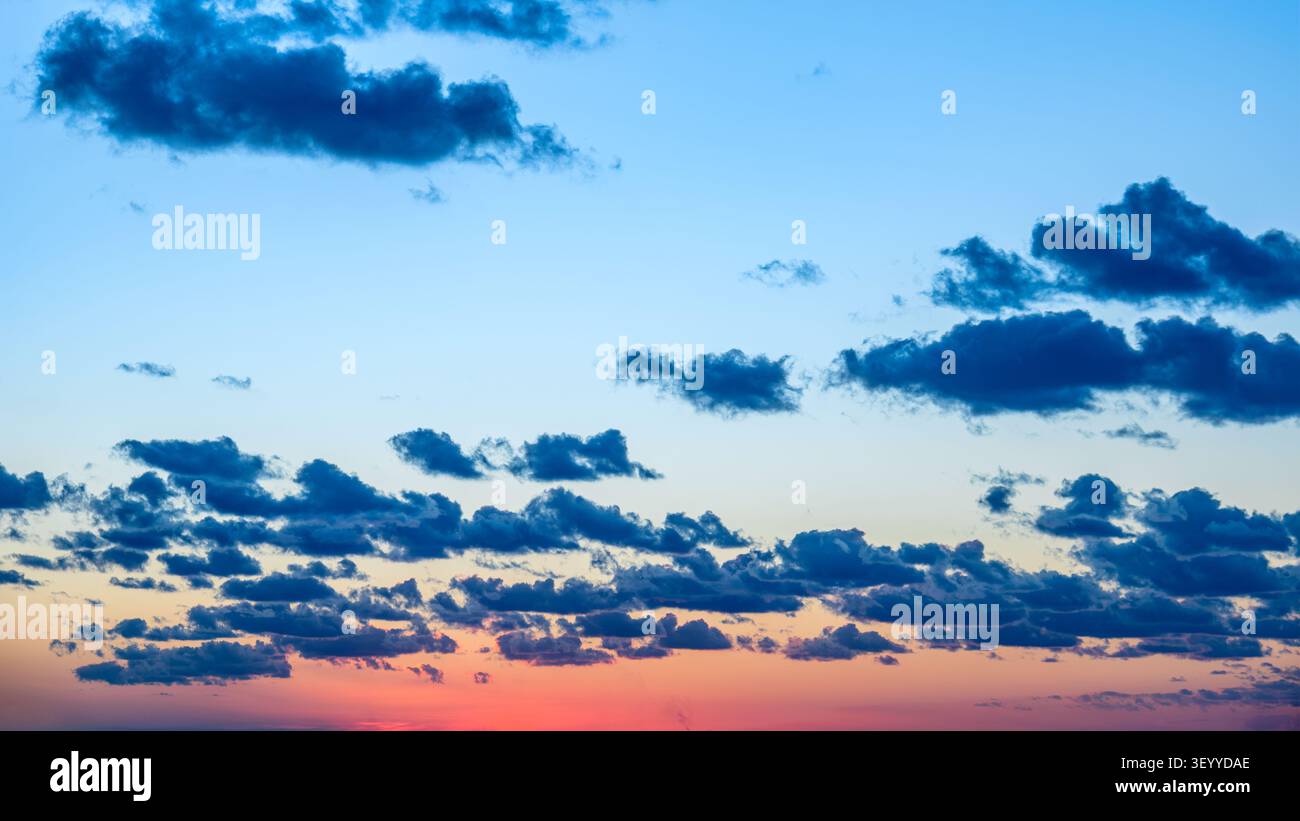 Cielo colorato al tramonto con nuvole sparse all'orizzonte al tramonto vicino a un paesaggio tranquillo. Foto Stock