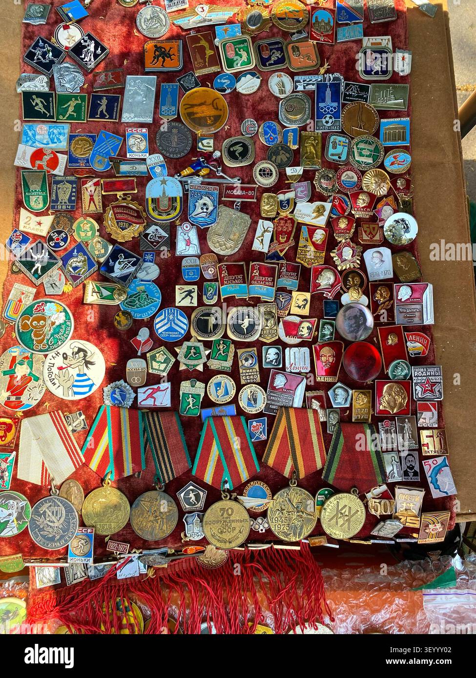 Kableshkovo, Bulgaria - 2 luglio 2026: Medaglie, distintivi e spille vintage disposte su velluto rosso in un mercato delle pulci, mettendo in risalto diversi design e stile storico Foto Stock