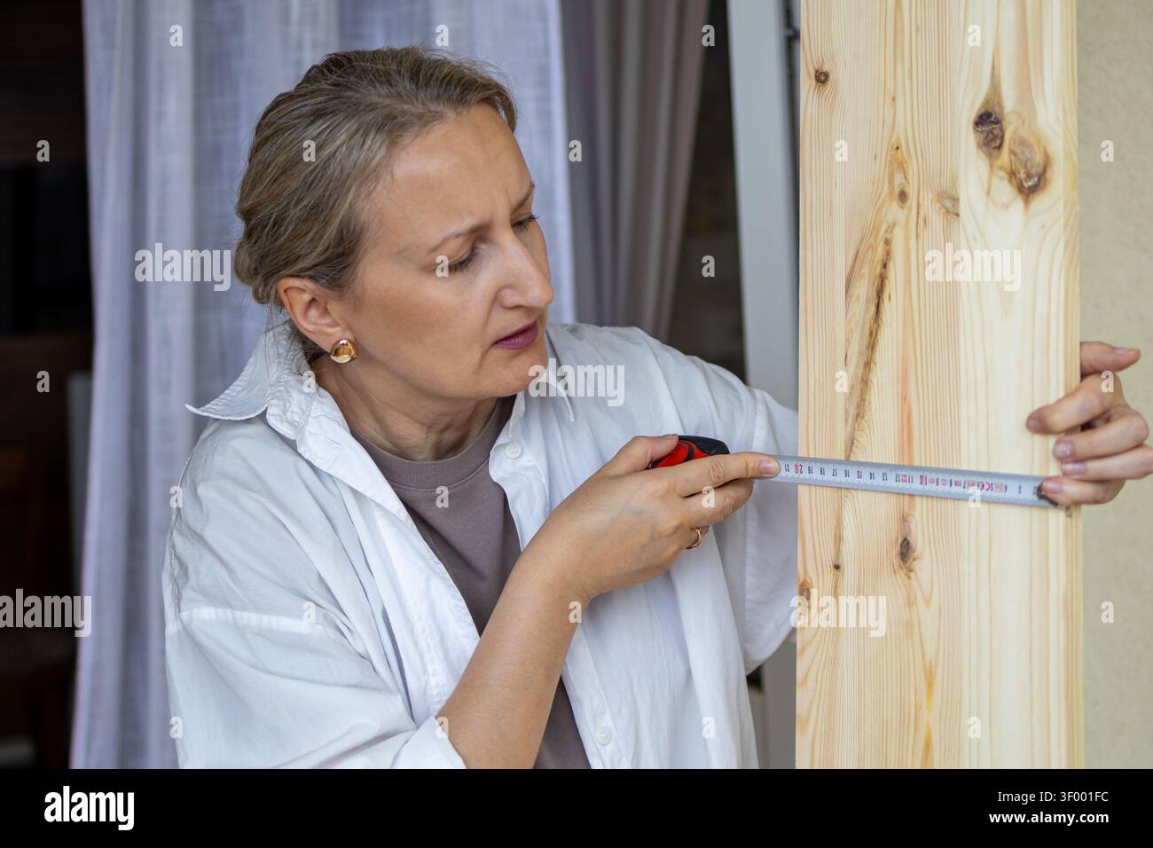 Donna misura un pannello di legno con un metro a nastro prima di tagliare e assemblare mobili a casa. Concetto di precisione, lavorazione del legno fai da te, scarico femminile Foto Stock