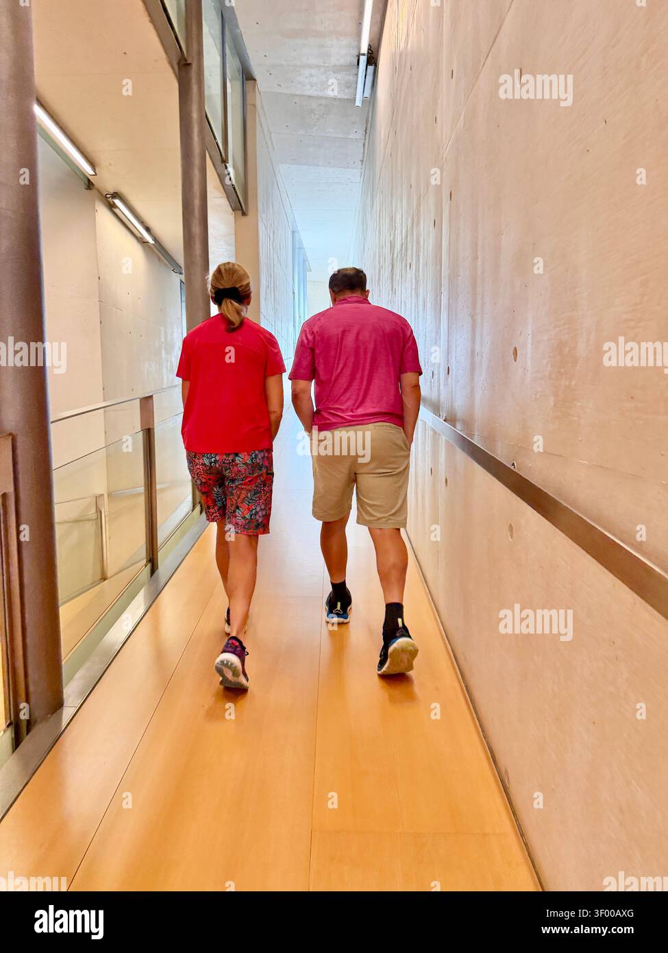 Vista posteriore di un uomo e di una donna che camminano attraverso un moderno corridoio di cemento con pavimenti in legno - Immagine stock catturata con smartphone