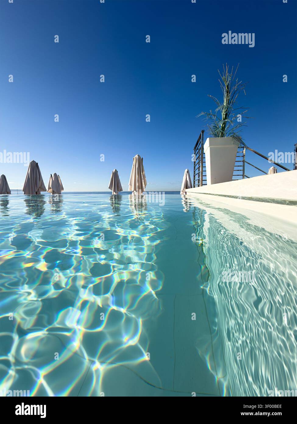 Vista a livello dell'acqua di una piscina a sfioro con ombrelloni chiusi e cielo azzurro Palma di Maiorca Foto Stock