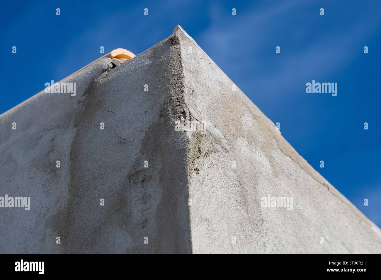 Una vista dettagliata di un angolo della parete esterna che mostra cemento testurizzato e un tetto in terracotta contro un cielo luminoso e senza nuvole Foto Stock