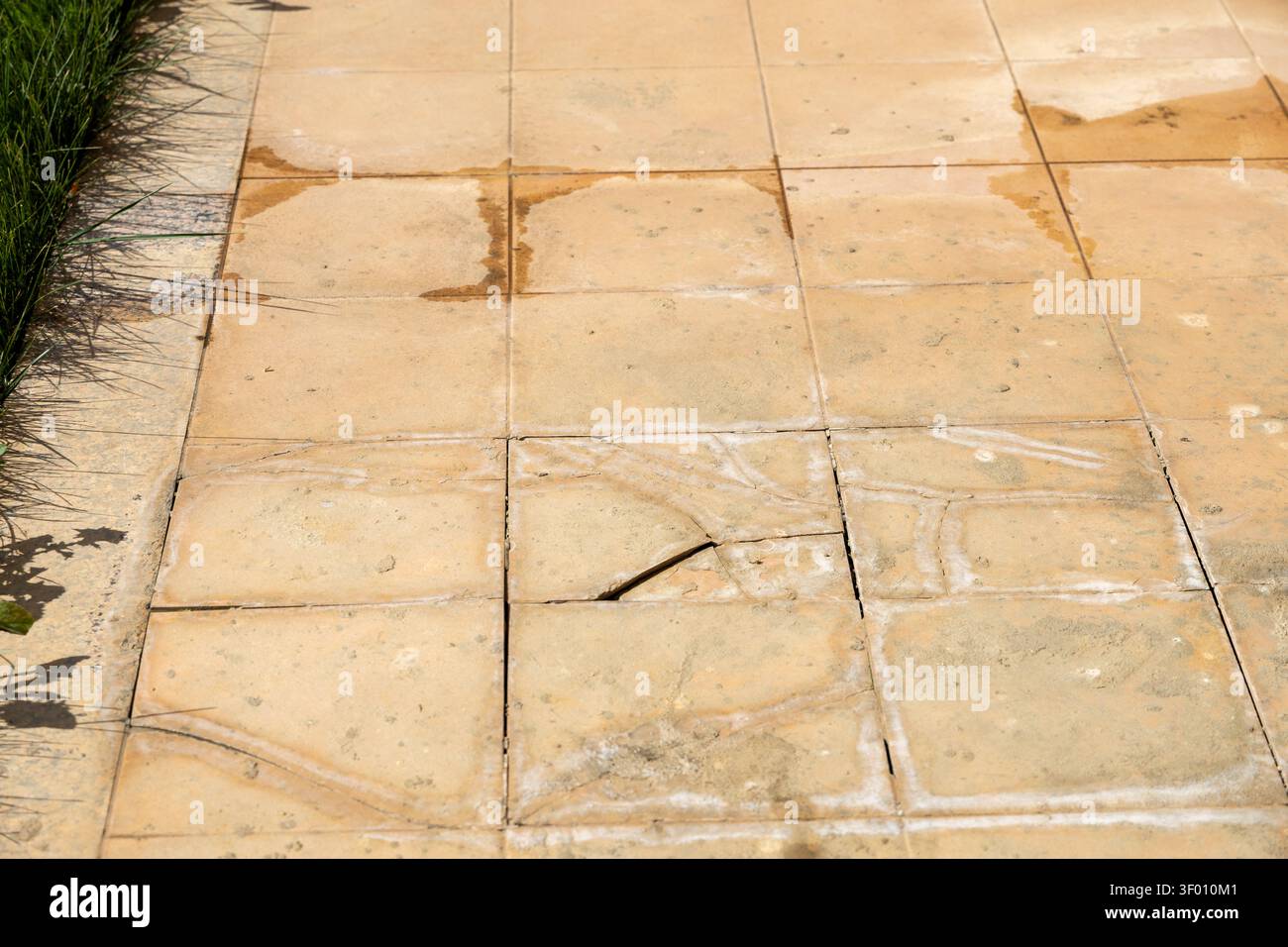 Vista ravvicinata delle pietre di pavimentazione beige intemprate su un patio esterno, evidenziando segni di età e danni come segni d'acqua e superfici fratturate Foto Stock